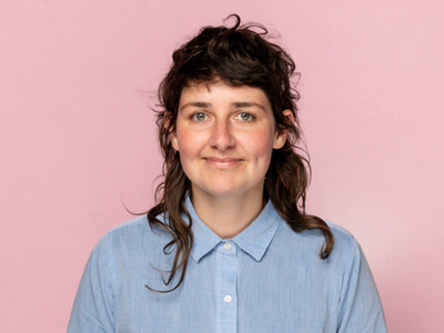 Non-binary person smiling wearing purple in front of a pink background